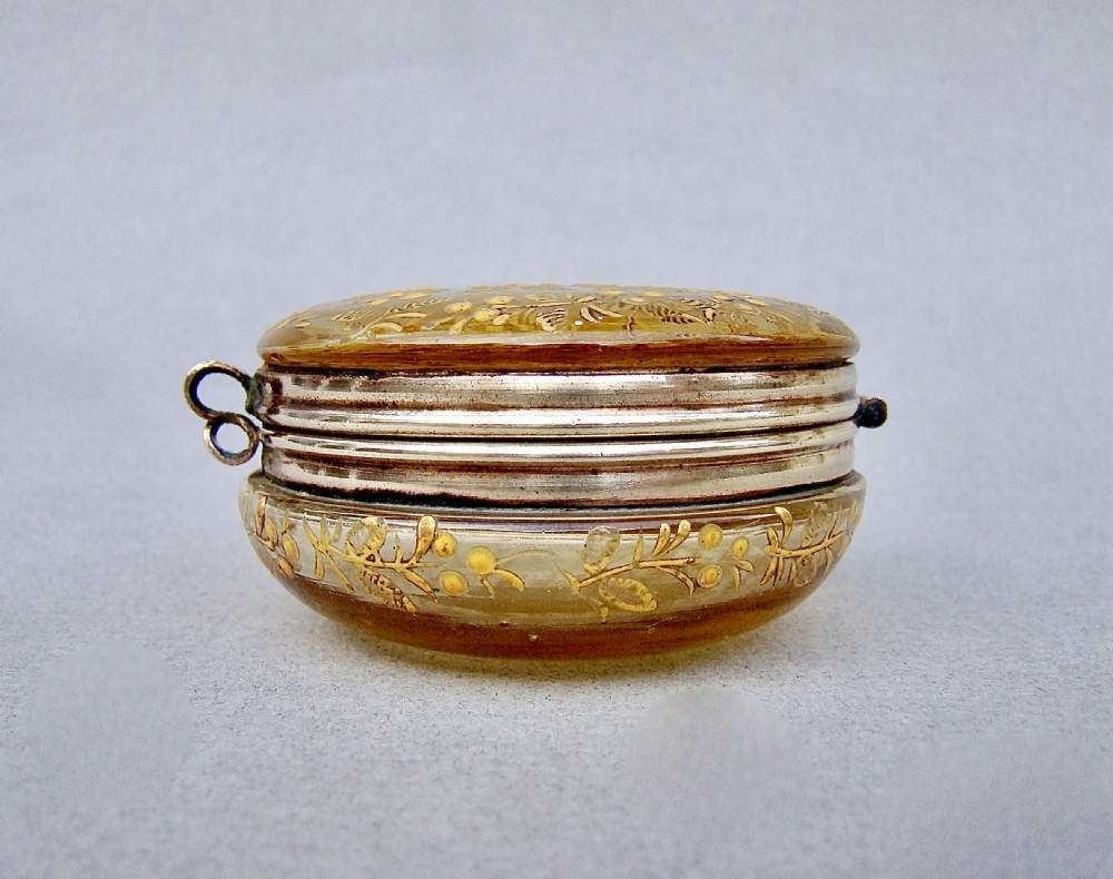 A circular amber glass trinket box decorated with detailed gilt enamel floral motifs and a hinged metal frame. View IV