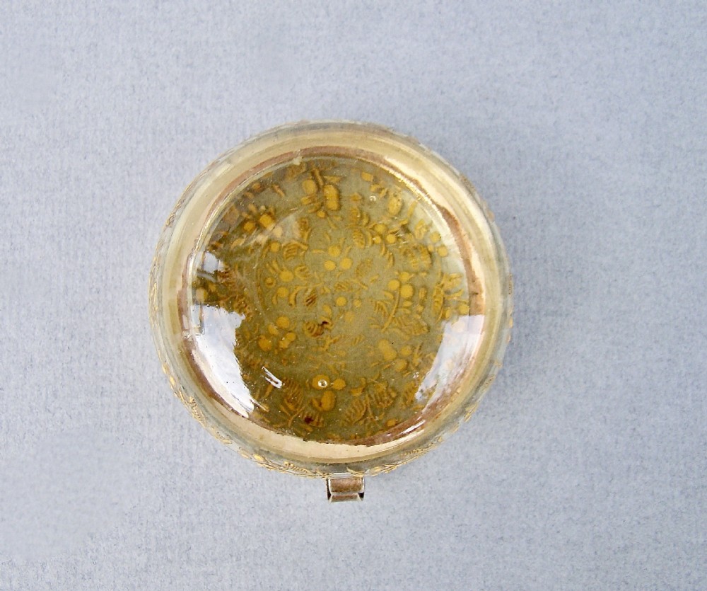 A circular amber glass trinket box decorated with detailed gilt enamel floral motifs and a hinged metal frame. View VI