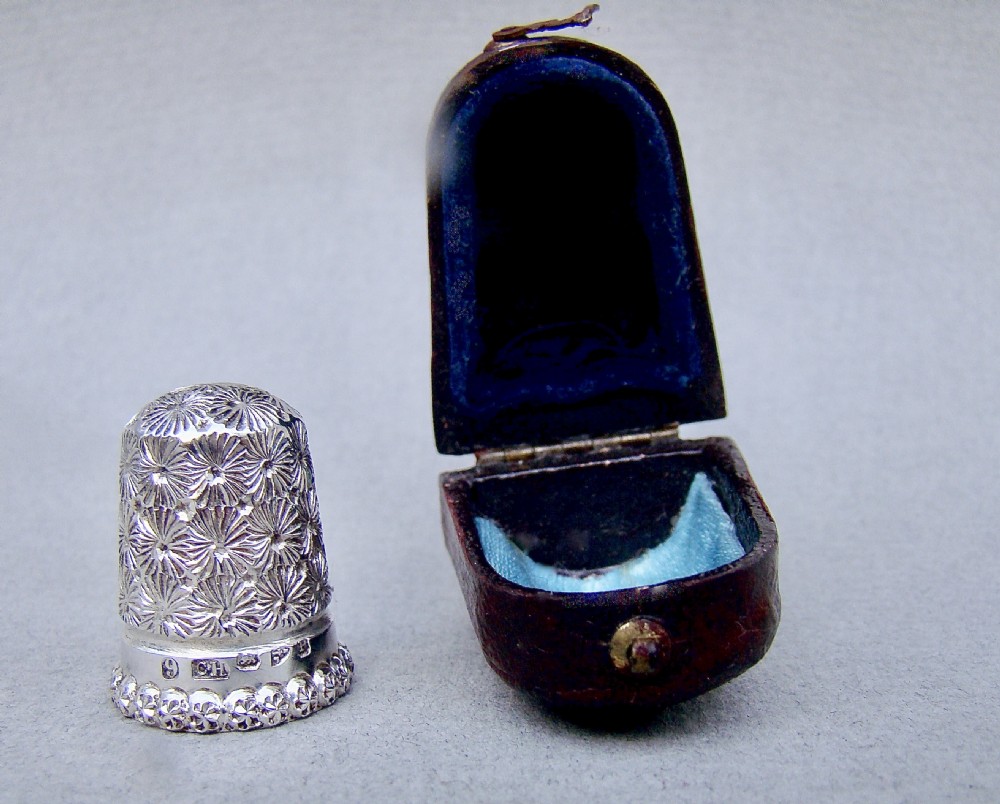 A hallmarked Victorian sterling silver thimble with a starburst textured pattern displayed beside its original blue-lined fitted leather case. View VI