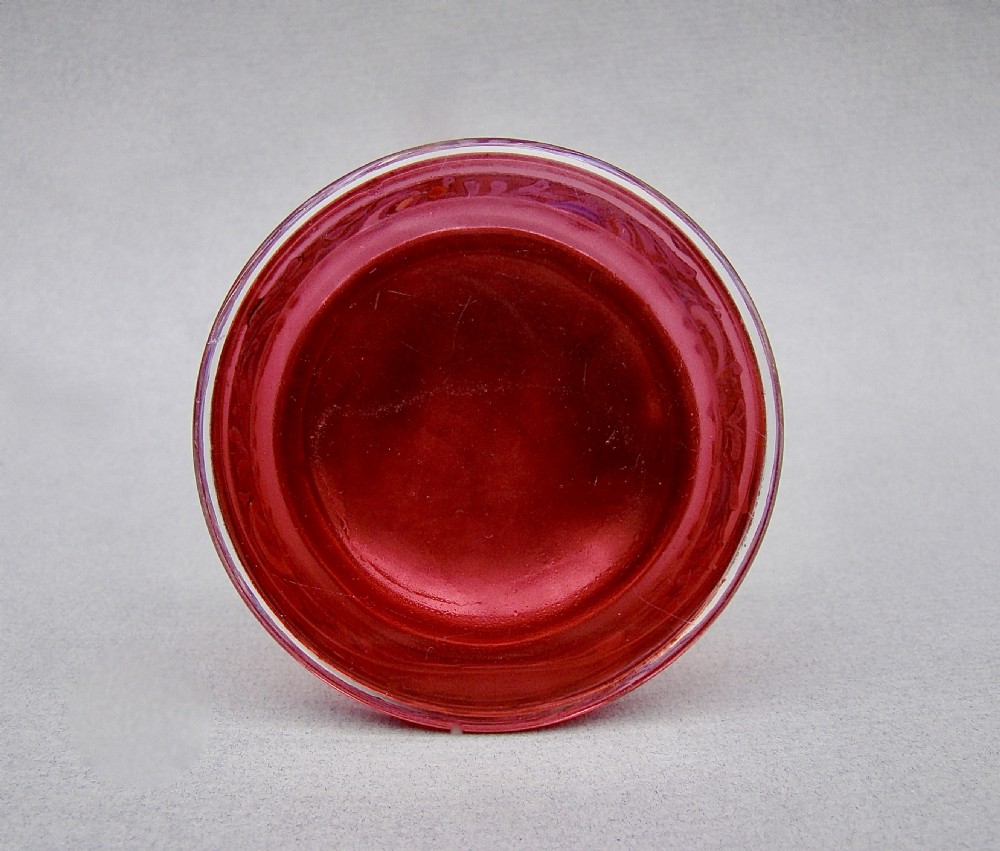 A small circular cranberry glass trinket box decorated with purple and blue enamelling, topped with a plain polished sterling silver lid. View V