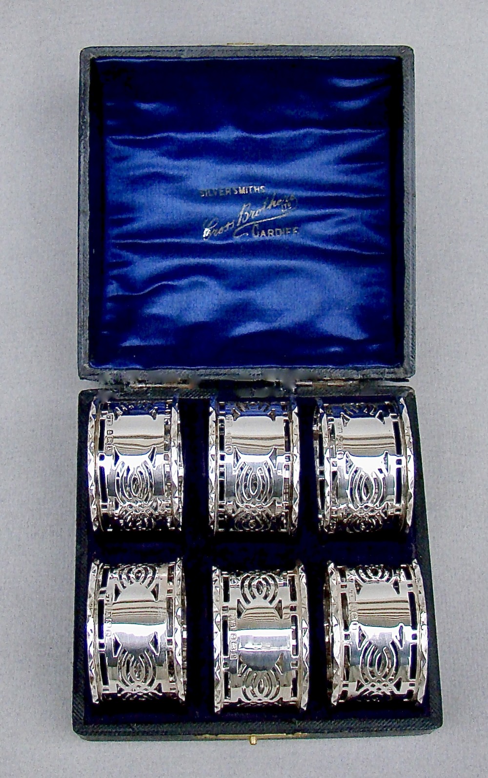 A cased set of six sterling silver napkin rings with pierced geometric decoration, presented inside a dark velvet and silk lined box.