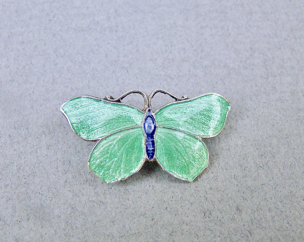 An Art Deco silver butterfly brooch featuring light green translucent enamel wings and a dark blue enamel body.