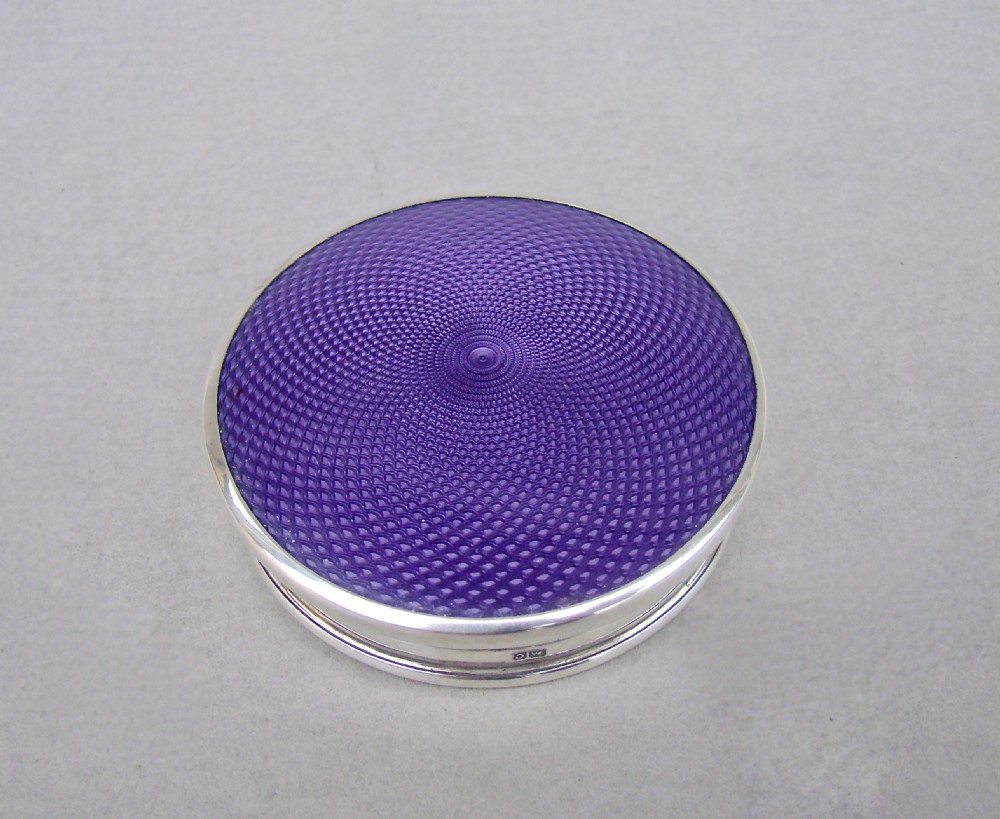 A circular Art Deco sterling silver powder compact featuring a purple engine-turned textured top.