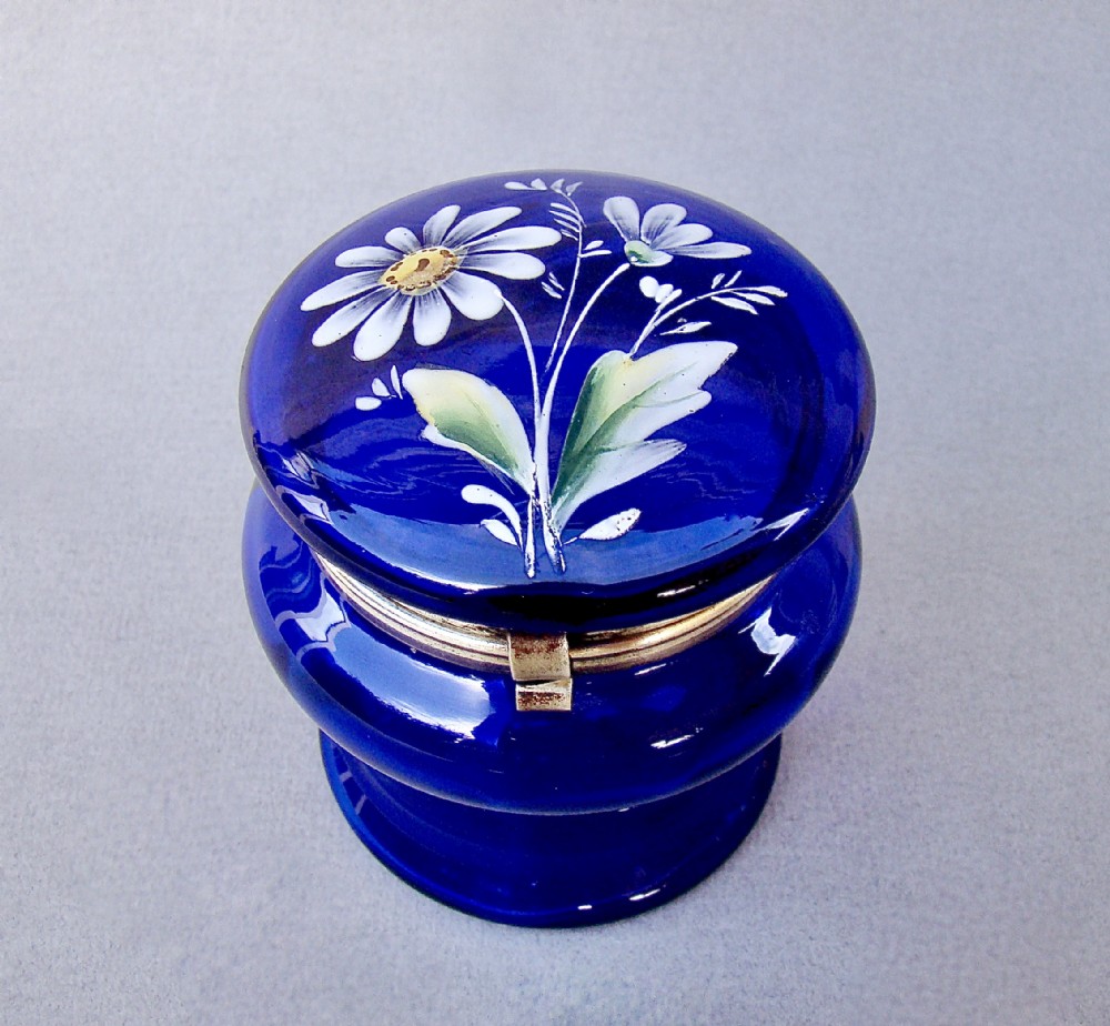A deep cobalt blue glass dressing table jar featuring hand-painted white daisy enamel decoration and a hinged metal rim.