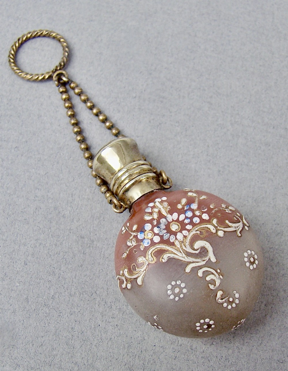 A nineteenth-century French satin glass chatelaine scent bottle decorated with hand-applied enamel scrolls and flowers, fitted with a gilded metal cap and chain.