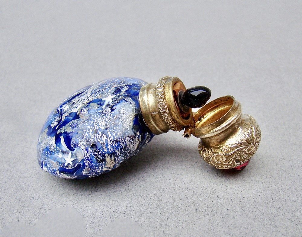 A round cobalt blue Murano glass scent bottle featuring swirl patterns, silver leaf inclusions, star murrine, and an embossed silver-gilt cap set with a red gemstone. View IV