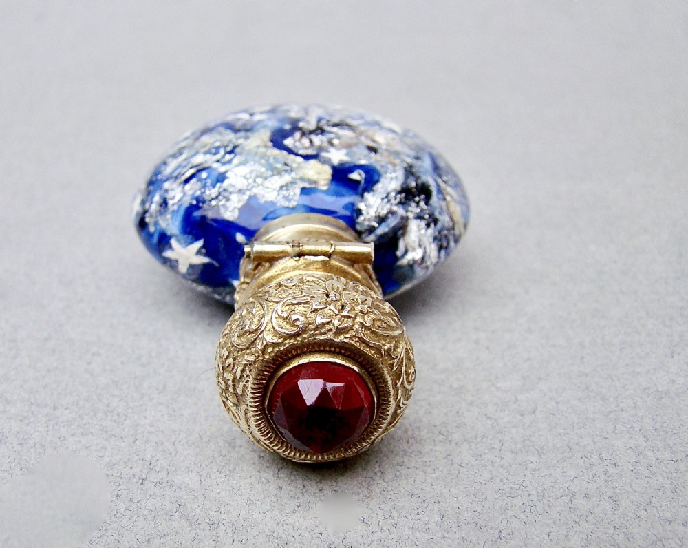 A round cobalt blue Murano glass scent bottle featuring swirl patterns, silver leaf inclusions, star murrine, and an embossed silver-gilt cap set with a red gemstone. View VII