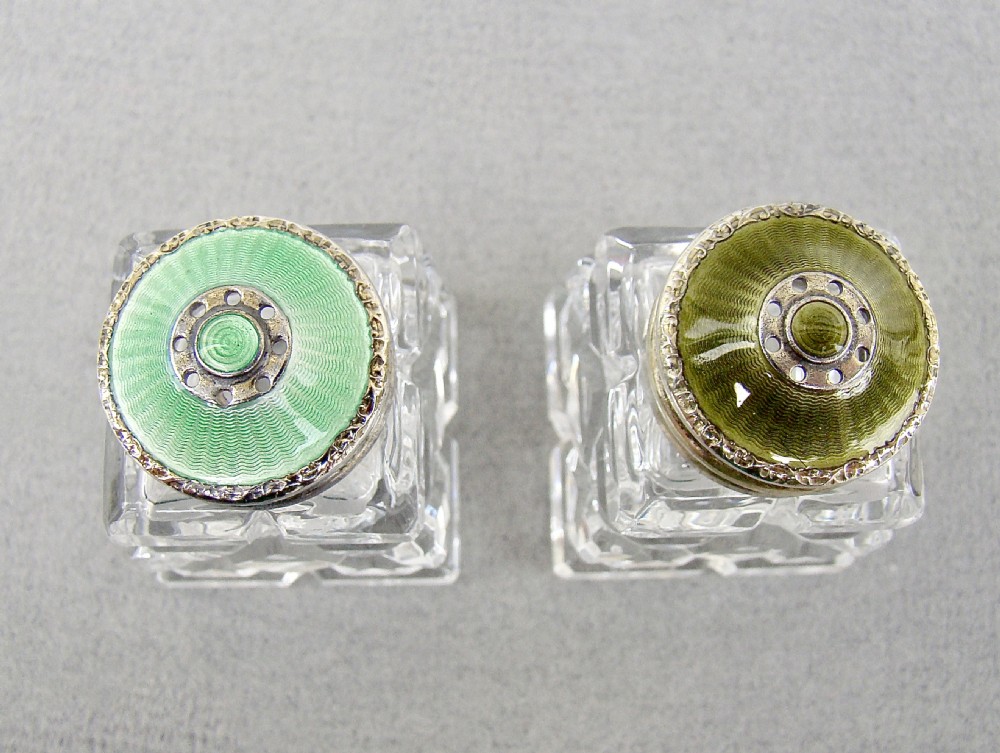 A pair of Art Deco cut glass salt shakers featuring green guilloche enamel and silver tops, shown in front of their fitted presentation box. View IV