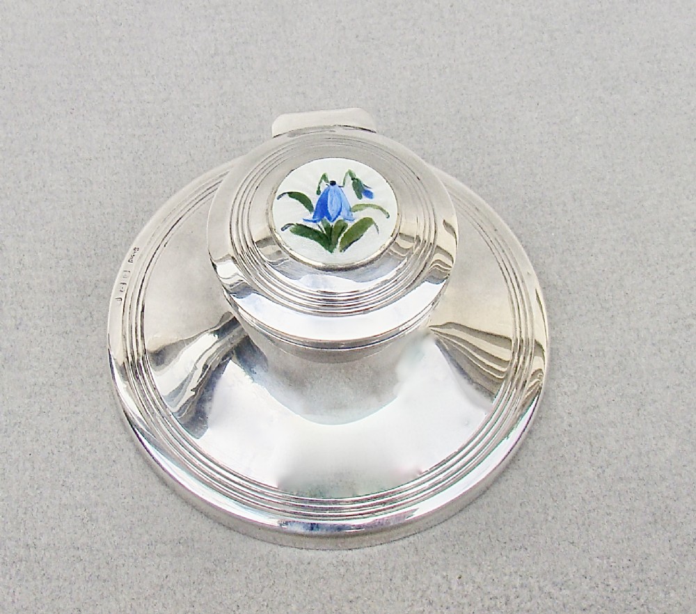 A circular Edwardian sterling silver capstan inkwell featuring a hinged lid inset with a floral guilloche enamel medallion.