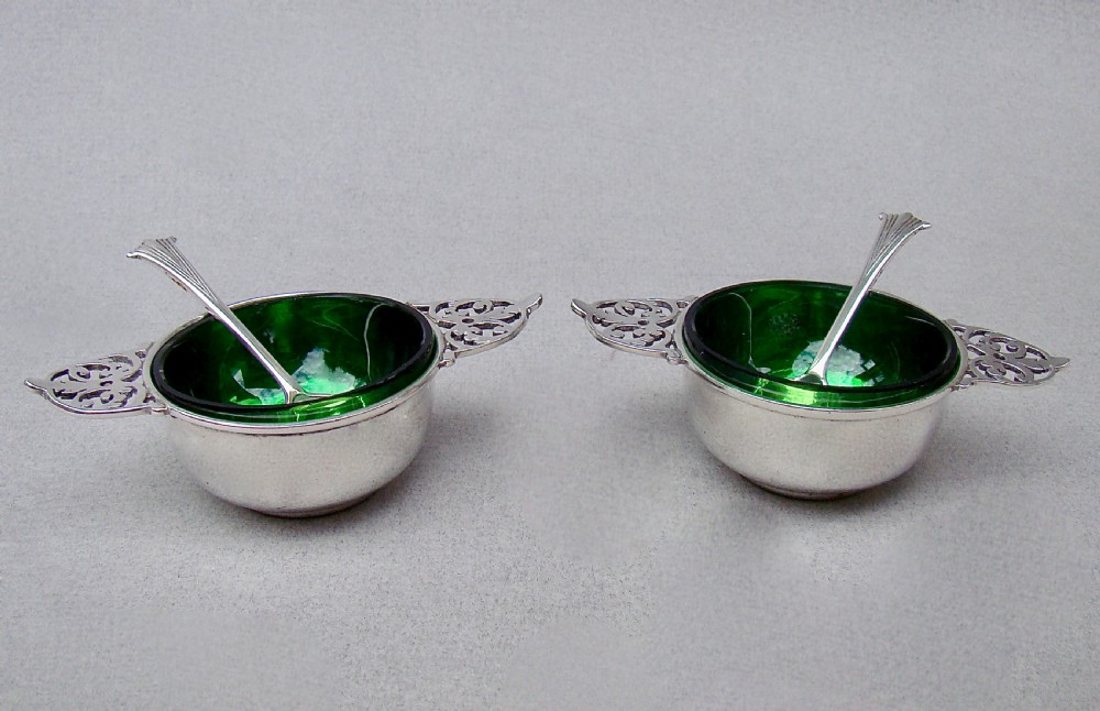 A pair of sterling silver quaich-form open salt cellars with pierced handles, vivid green glass liners, and two matching silver salt spoons. View IV
