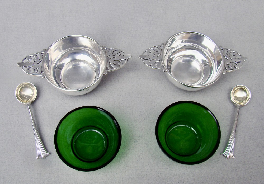 A pair of sterling silver quaich-form open salt cellars with pierced handles, vivid green glass liners, and two matching silver salt spoons. View V