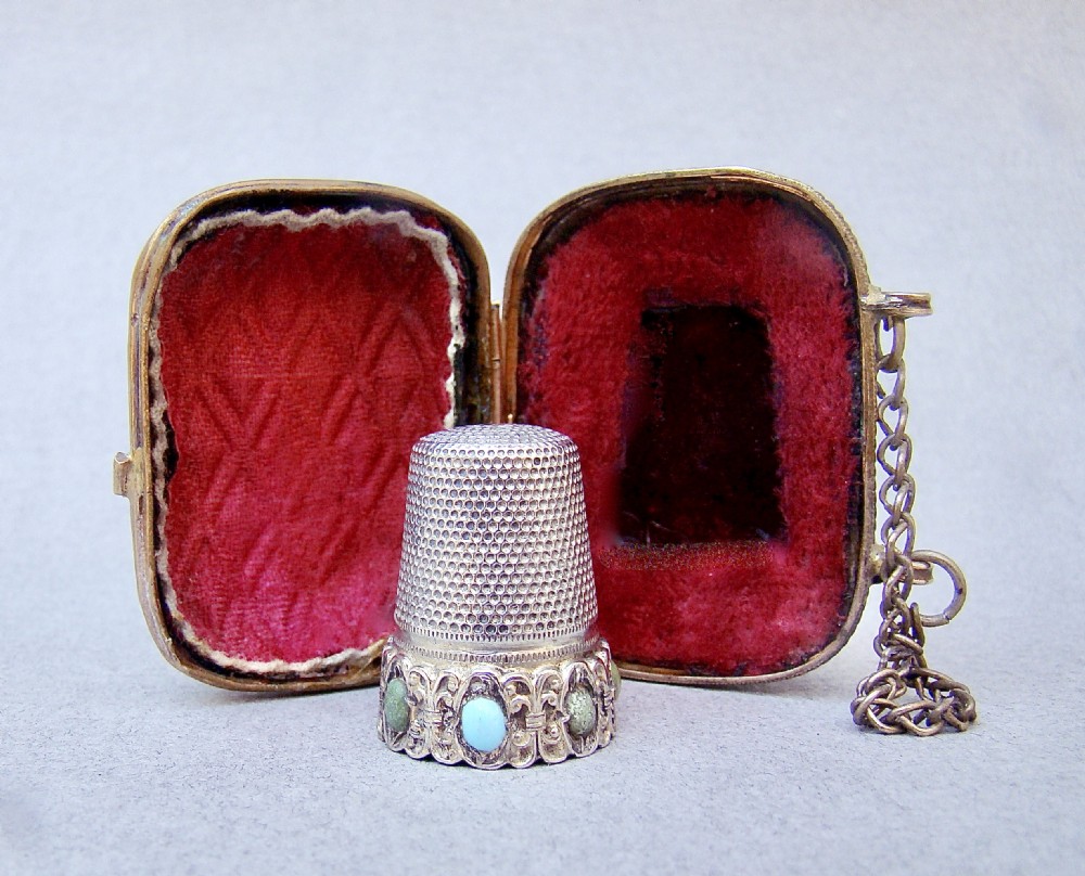 A 19th-century French silver thimble set with cabochon stones resting inside an open gilt ormolu presentation case with crimson velvet lining. View II
