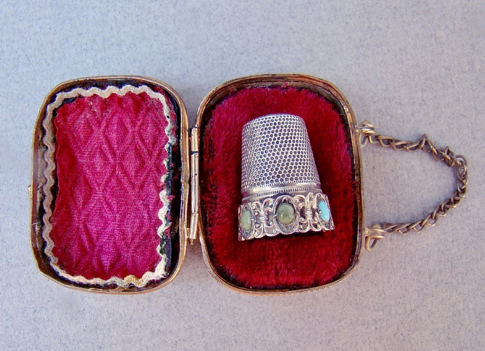 A 19th-century French silver thimble set with cabochon stones resting inside an open gilt ormolu presentation case with crimson velvet lining.