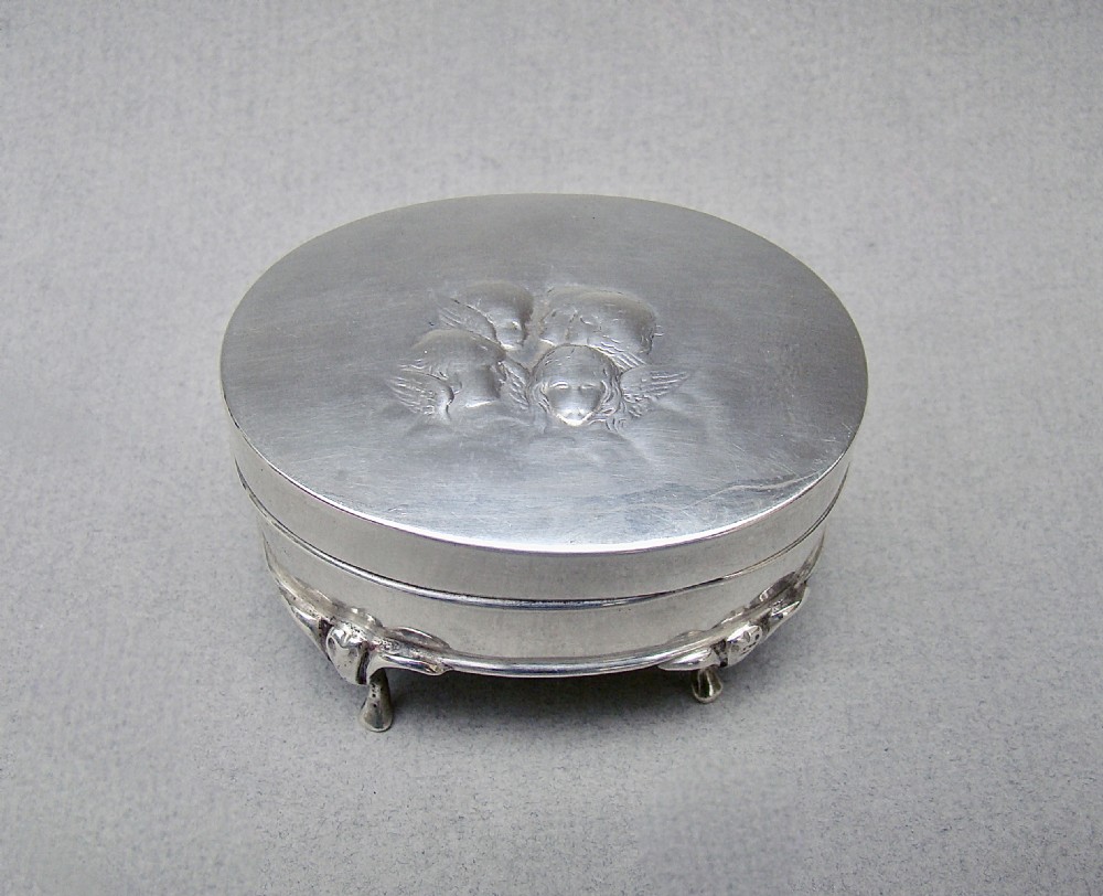 An oval Edwardian sterling silver jewellery box raised on four cast feet with an embossed cherub motif on the lid.