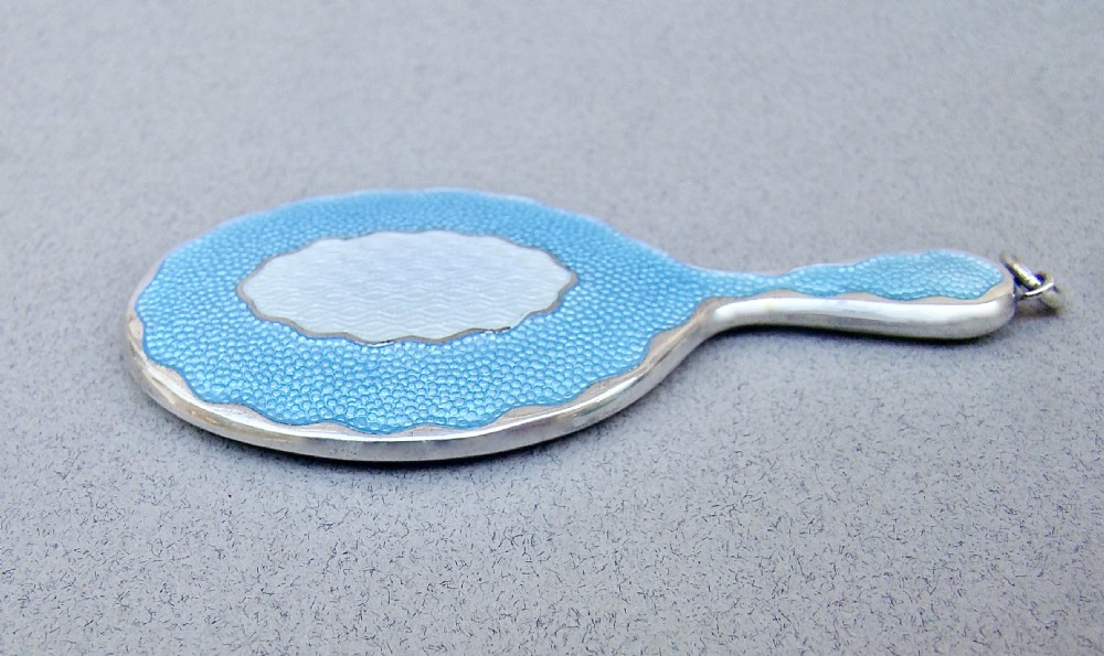 An Art Deco miniature sterling silver hand mirror featuring a scalloped rim, sky blue and white guilloche enamel, and a suspension ring. View IV