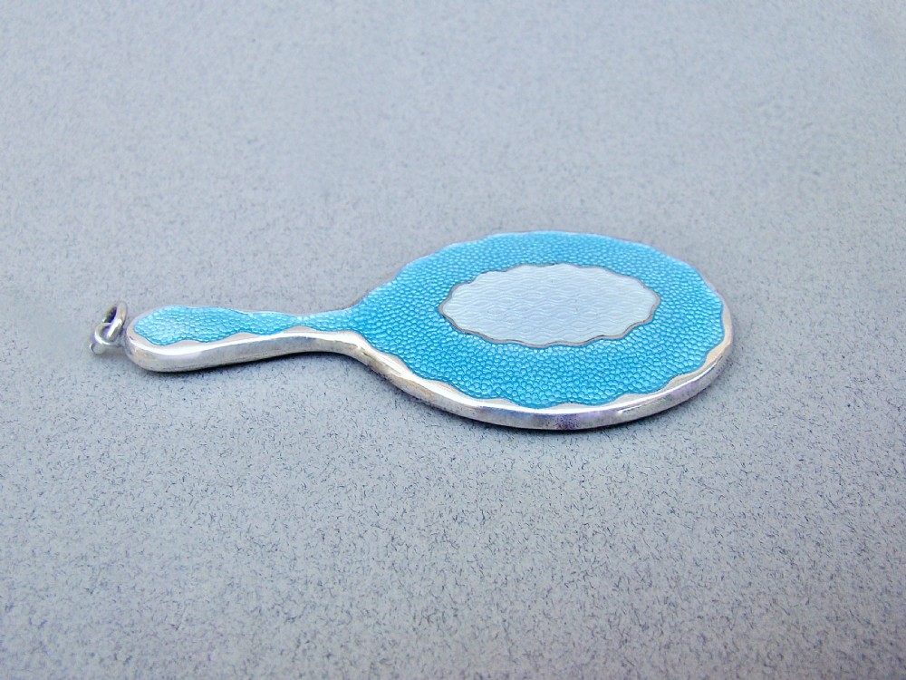 An Art Deco miniature sterling silver hand mirror featuring a scalloped rim, sky blue and white guilloche enamel, and a suspension ring. View V