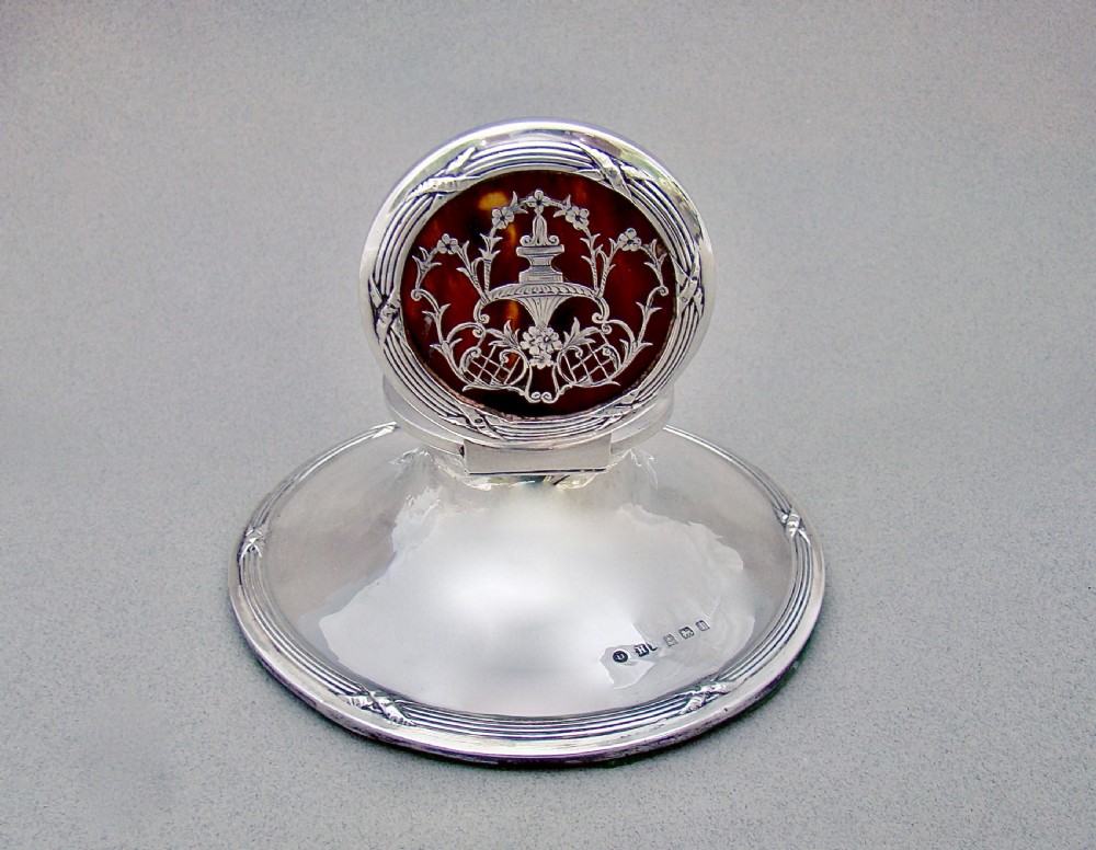 An Edwardian sterling silver capstan inkwell featuring a circular tortoiseshell lid inlaid with silver urn and garland motifs. View II