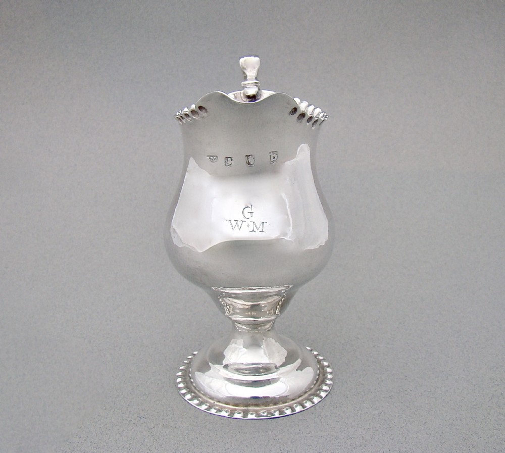 A Georgian sterling silver cream jug featuring a baluster shape, beaded rim, pedestal base, and engraved initials, assayed in London in 1777.