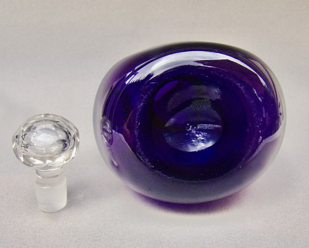 A Victorian bulbous amethyst purple glass decanter featuring an embossed silver collar, a clear glass handle, and a faceted clear glass stopper. View VIII