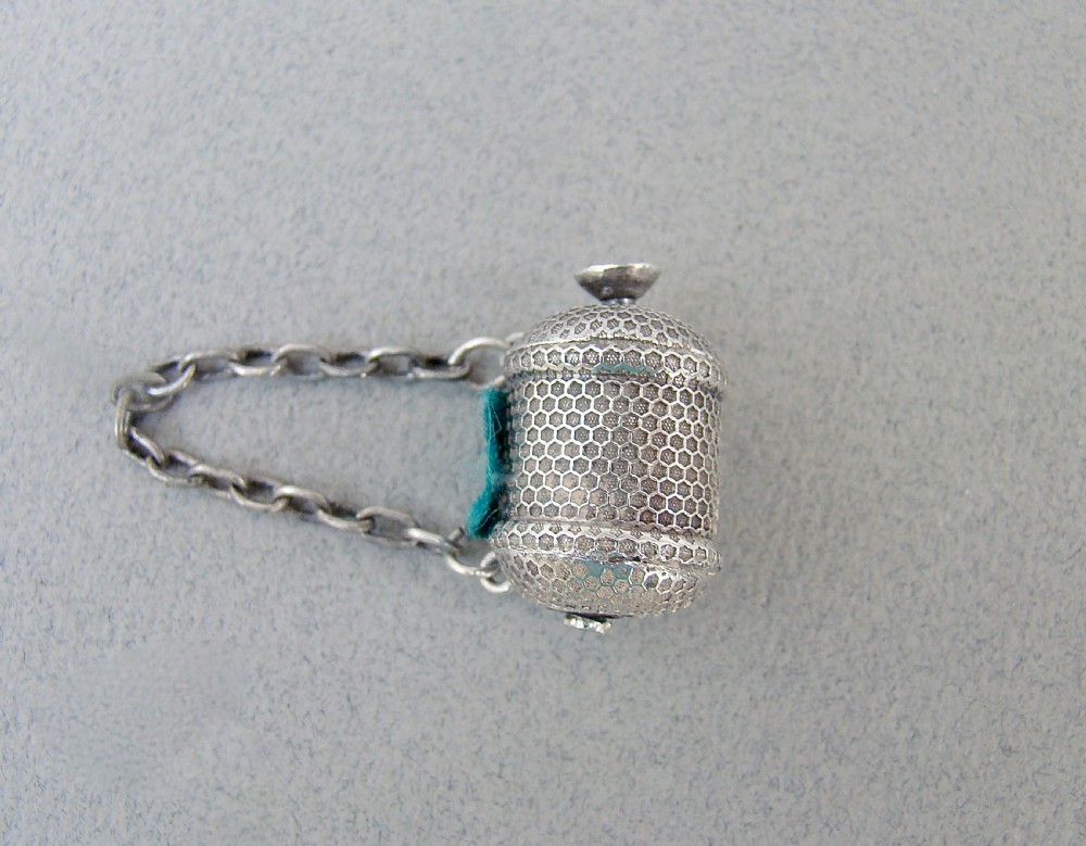 A drum-shaped Georgian silver tape measure with an engine-turned honeycomb texture and attached suspension chain.
