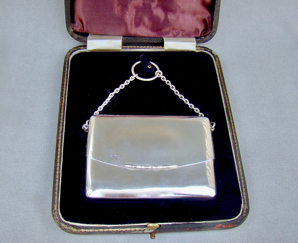 An Edwardian sterling silver card case designed in the shape of an envelope with a suspension chain, resting inside a velvet-lined fitted box. View VIII