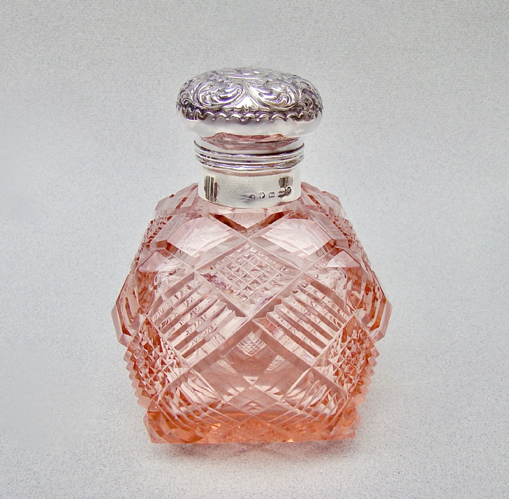 A Victorian pale salmon pink cut glass scent bottle featuring a hand-chased sterling silver top.