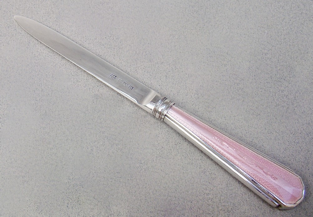 An Art Deco sterling silver letter opener featuring a tapered blade with English hallmarks and a pink guilloche enamel handle.