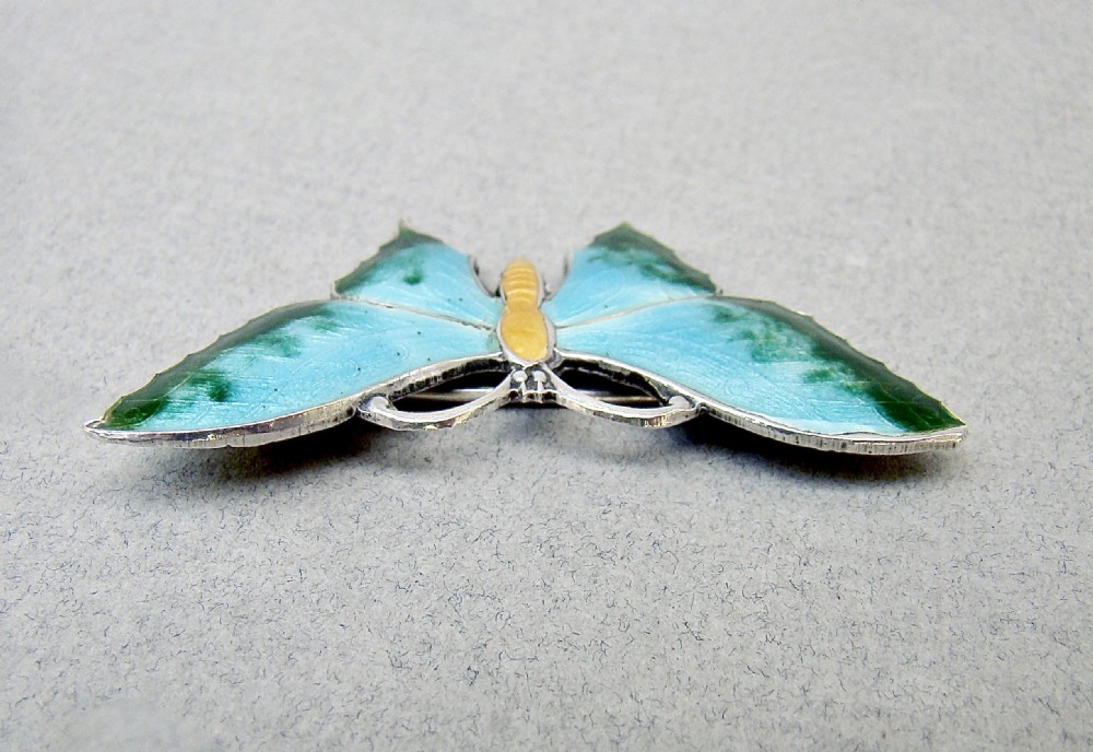 A Scandinavian sterling silver butterfly brooch featuring light blue and green guilloche enamel wings with a yellow body. View VI