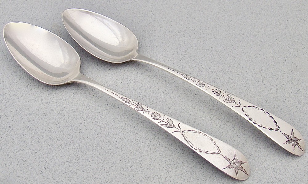 A pair of Georgian Irish sterling silver dessert spoons featuring bright-cut engraved stems with starburst and floral detailing.