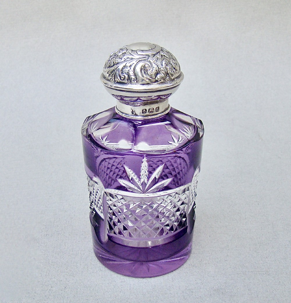 An Edwardian cut-to-clear amethyst glass scent bottle featuring diamond facets and an embossed sterling silver cap.
