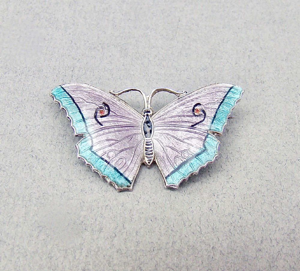 An Art Deco sterling silver and guilloche enamel butterfly brooch featuring lilac and turquoise wings with delicate engine-turned patterns.