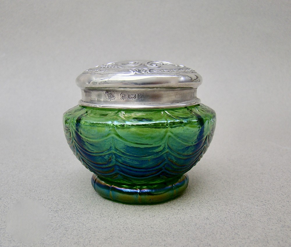 An antique green iridescent glass trinket pot with an embossed sterling silver lid.