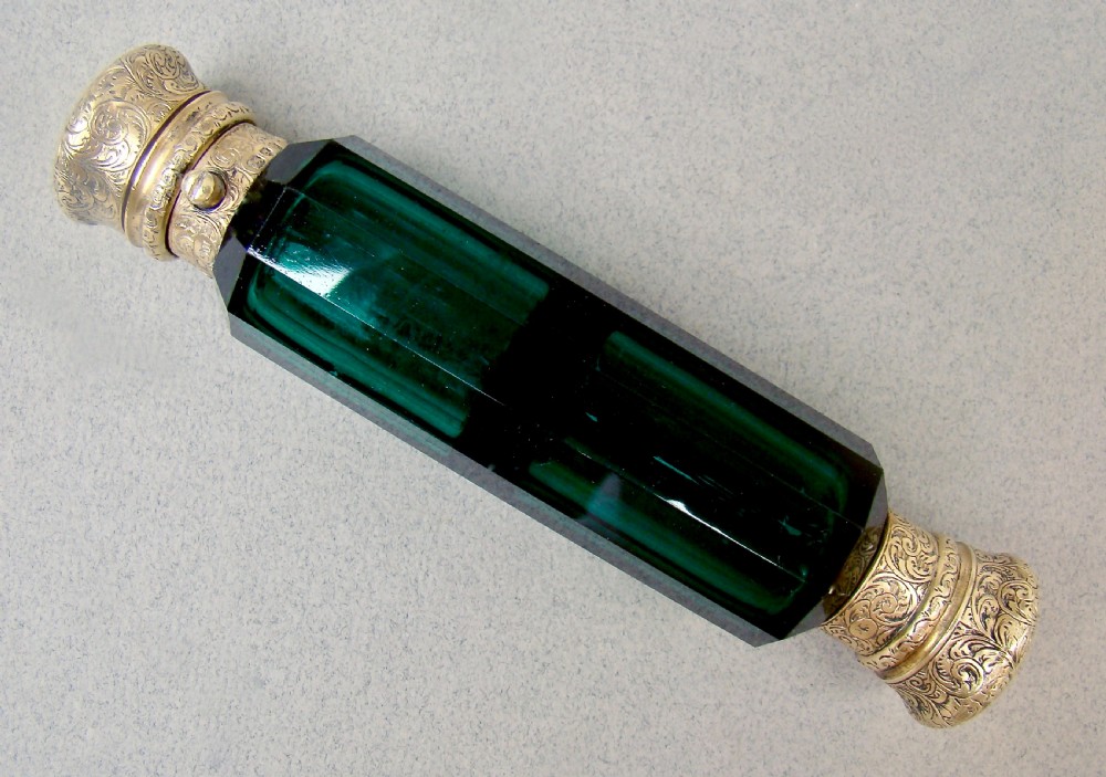 A Victorian double-ended faceted Bristol green glass scent bottle featuring intricately engraved silver-gilt caps on both ends.