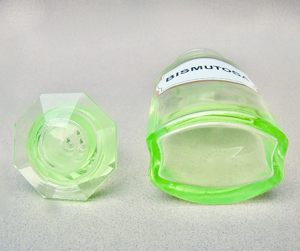 A light-green translucent uranium glass apothecary jar featuring a fitted faceted stopper and a printed label reading Bismutosa. View VI