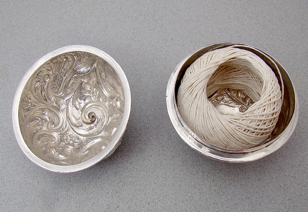 A spherical late Victorian sterling silver string box with chased floral and scroll ornamentation, resting on three ball feet with string extending from the top opening. View III