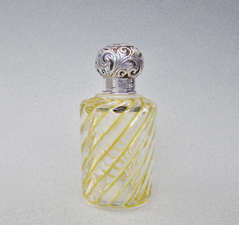 A clear glass cologne bottle featuring diagonal yellow swirl patterns, topped with a chased sterling silver stopper.