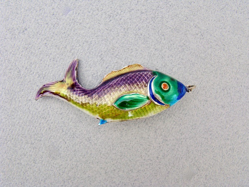 A silver fish-shaped pendant featuring green and purple guilloche enamel across the body and a suspension loop at the mouth.