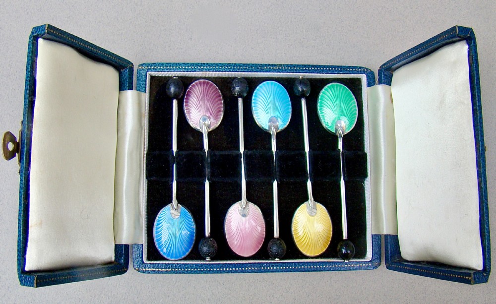 A cased set of six sterling silver coffee spoons featuring bean knops and engine-turned guilloche enamel bowls in various pastel colours.