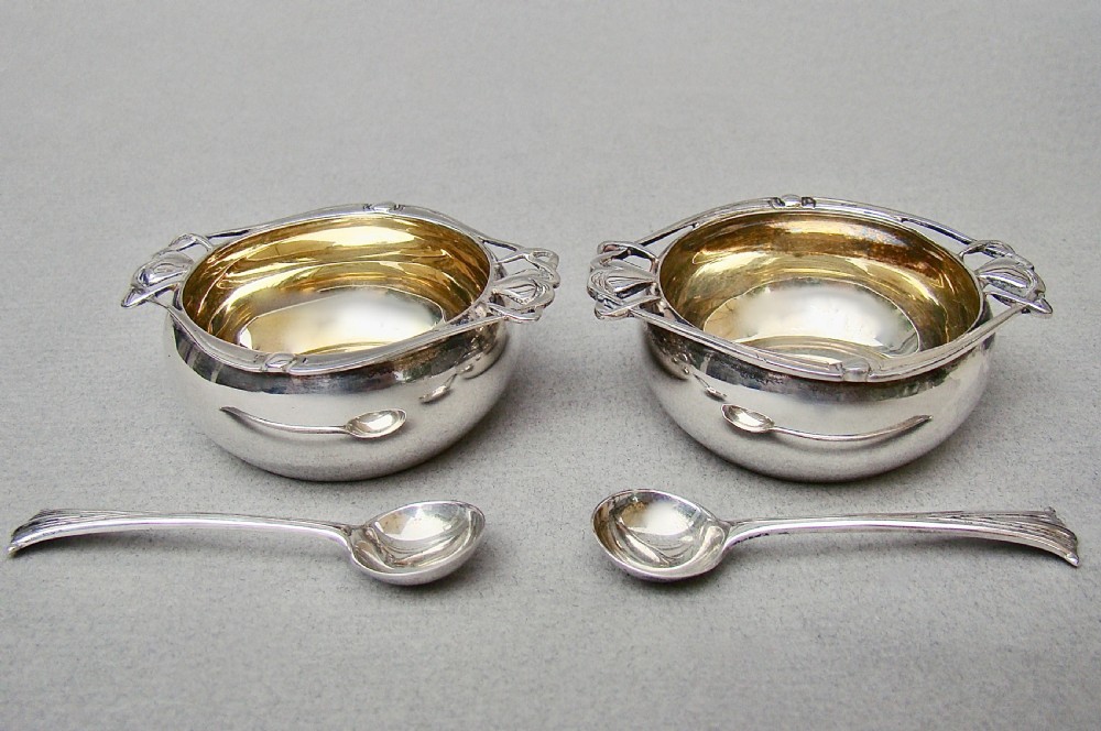 A cased pair of Edwardian sterling silver open salt cellars with stylised handles and matching spoons set in a purple velvet fitted presentation box. View III