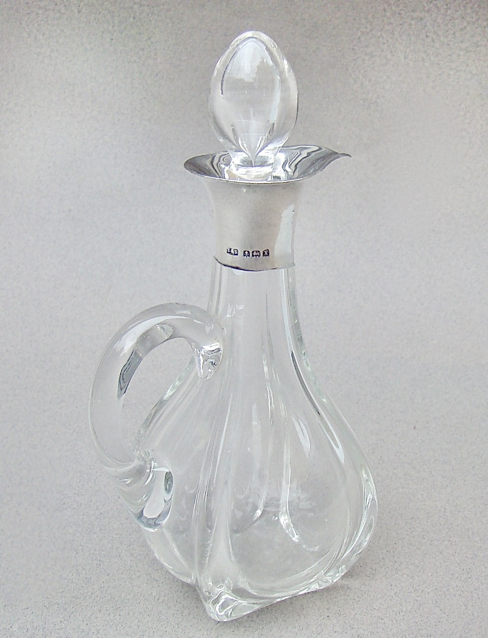 An Art Deco clear glass oil bottle with a silver-mounted rim, stopper, and integral handle.