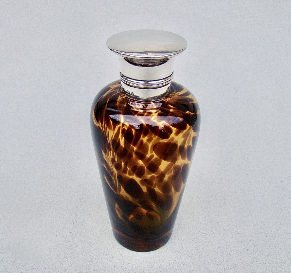 An Edwardian silver and tortoiseshell pattern glass scent bottle featuring a polished metal cap and a mottled amber brown tapered body.