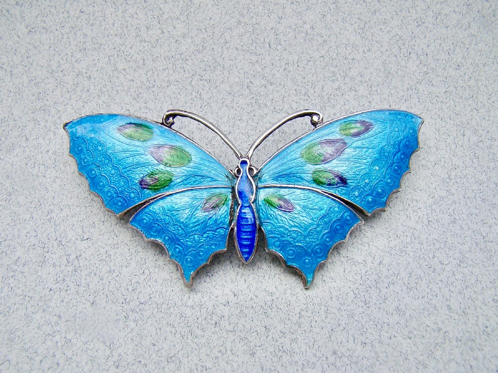 A Scandinavian sterling silver butterfly brooch featuring bright blue guilloche enamel wings with green and purple accents.