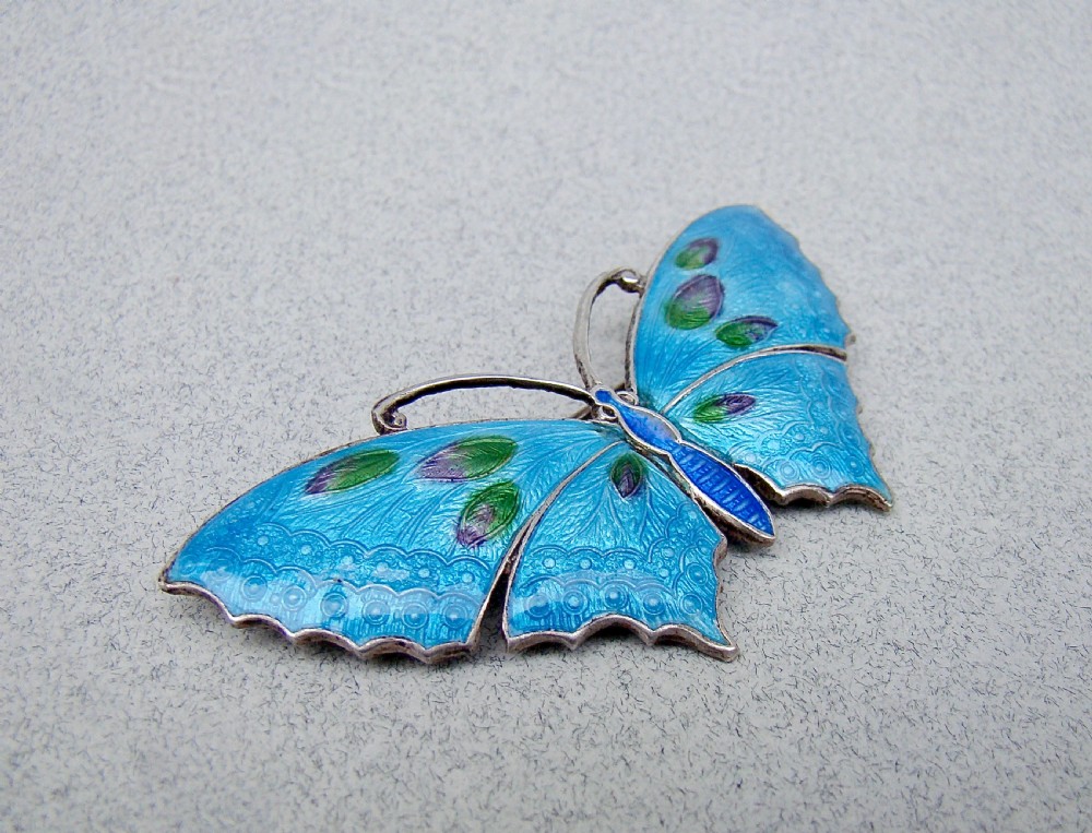 A Scandinavian sterling silver butterfly brooch featuring bright blue guilloche enamel wings with green and purple accents. View VI