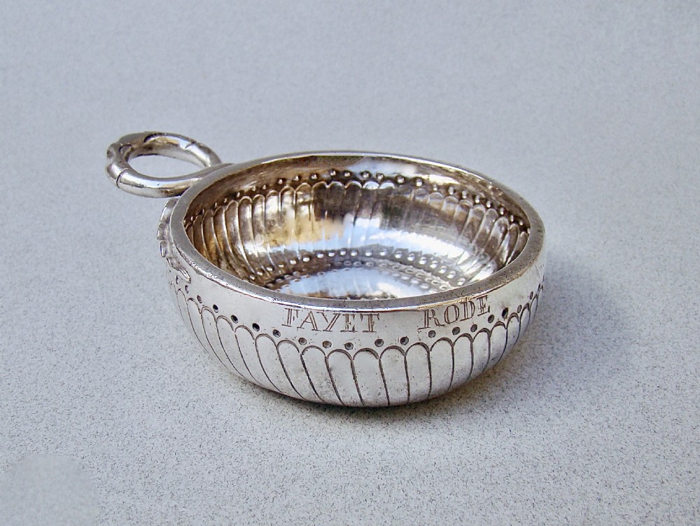 A shallow early 19th-century French silver wine taster featuring fluted gadrooning, punchwork detailing, engraved rim lettering, and a ring handle.