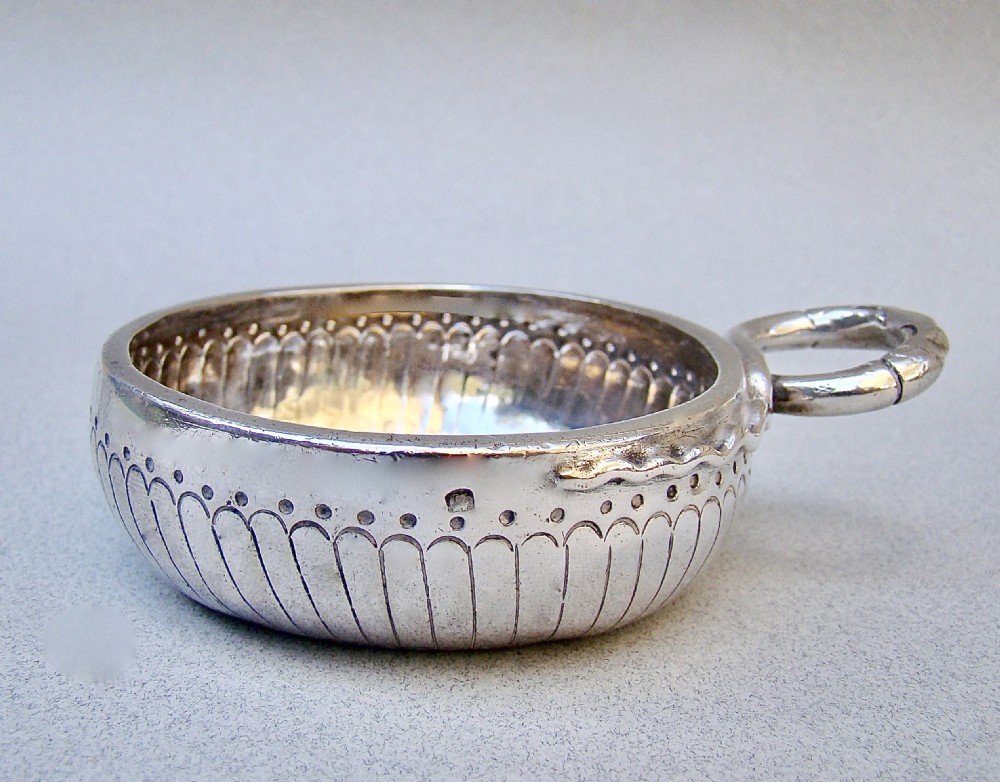A shallow early 19th-century French silver wine taster featuring fluted gadrooning, punchwork detailing, engraved rim lettering, and a ring handle. View II