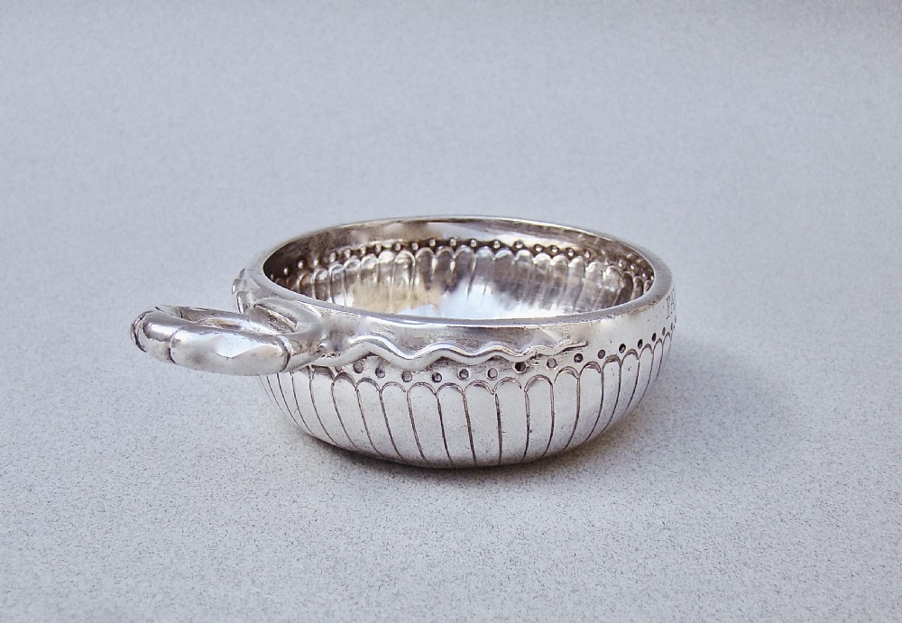 A shallow early 19th-century French silver wine taster featuring fluted gadrooning, punchwork detailing, engraved rim lettering, and a ring handle. View VII