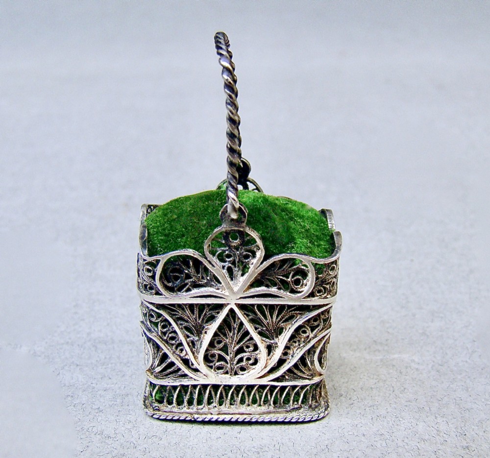 A Georgian silver filigree basket pin cushion with a twisted wire handle and a green velvet cushion pad.