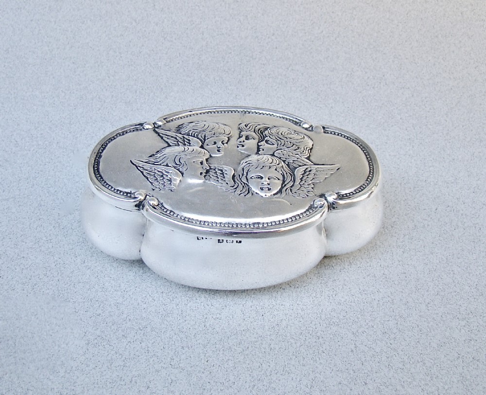An Edwardian sterling silver lobed trinket box with a hinged lid embossed with five cherub heads surrounded by a beaded border.