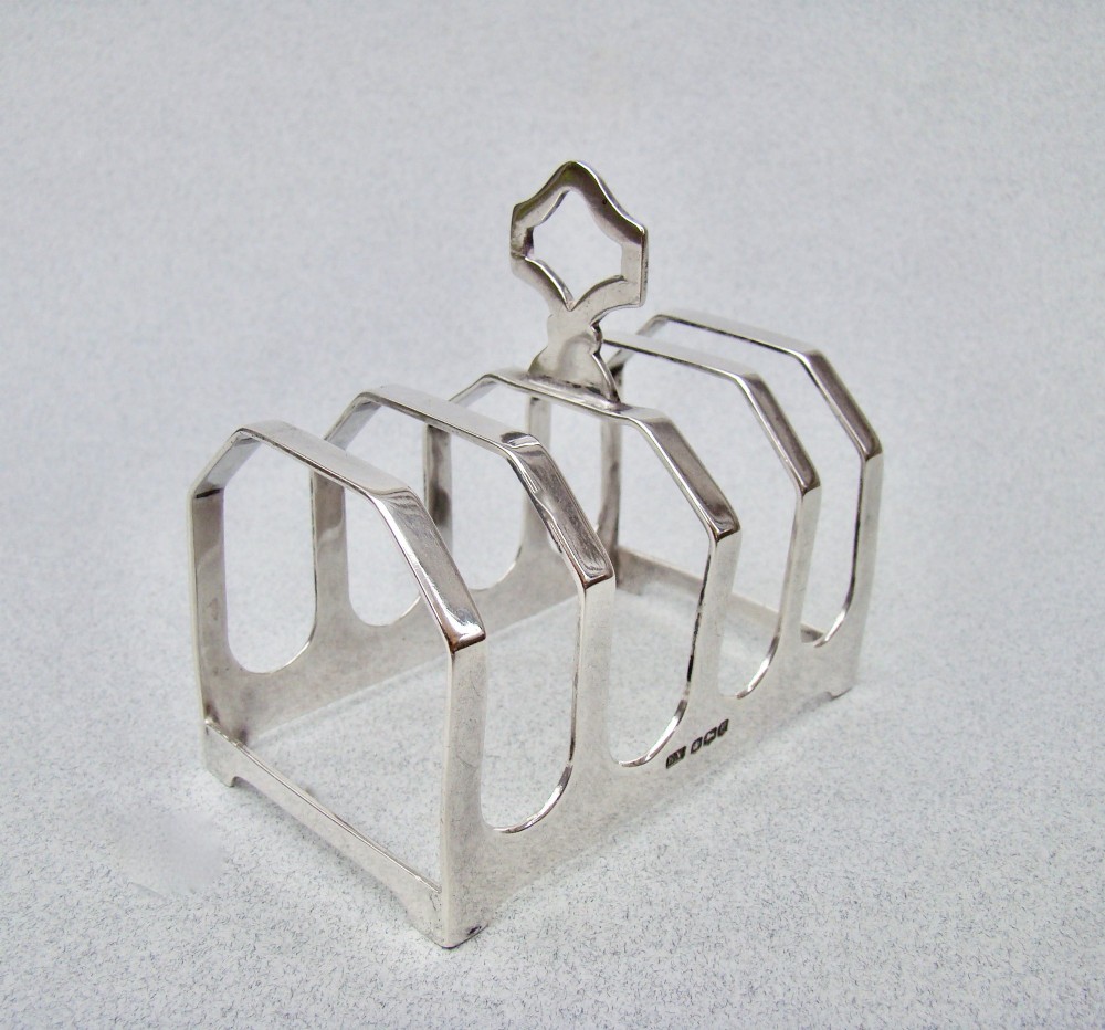 An Art Deco solid silver four-slice toast rack featuring angular dividers and a geometric central handle.