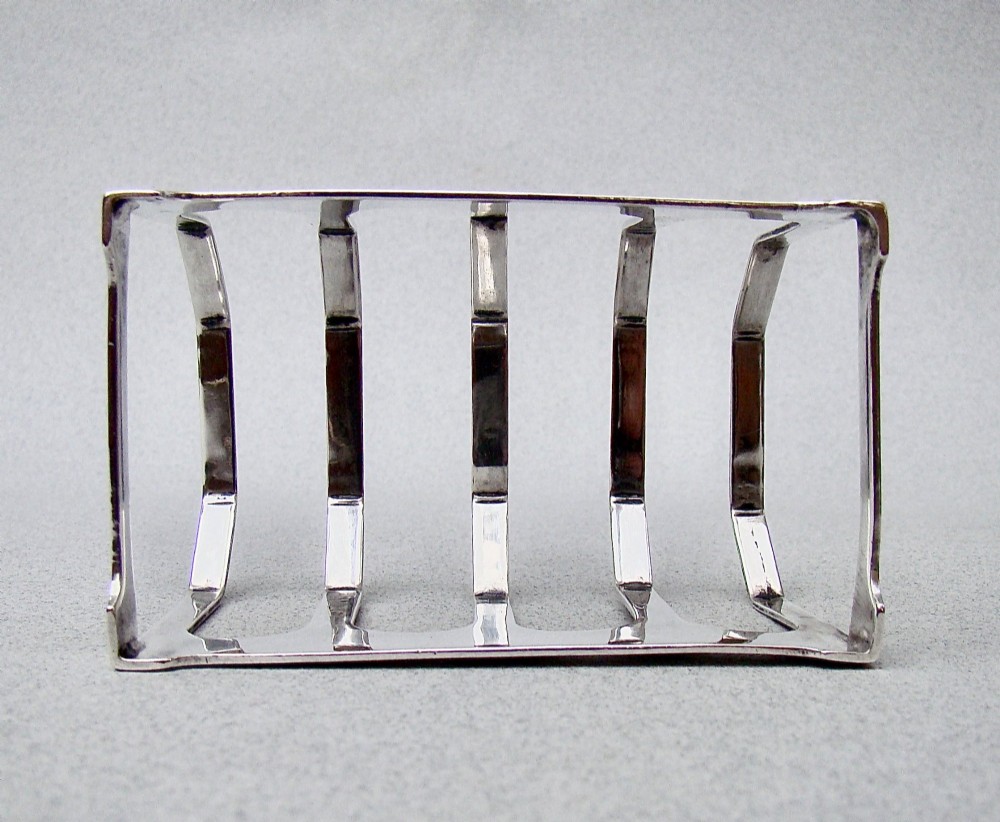 An Art Deco solid silver four-slice toast rack featuring angular dividers and a geometric central handle. View V